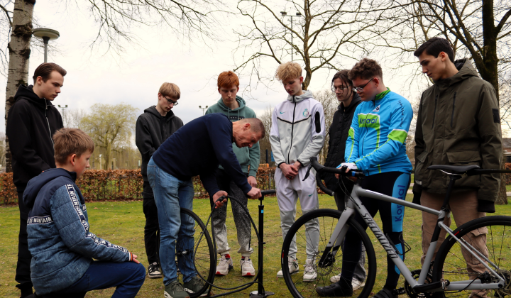 : De La Salle-wielrenners Sharvano, Stijn, Joris, Tobias, Raf, Elize, Zjuul en Keano (v.l.n.r.) kijken aandachtig hoe oud-wielerprof Pascal Hermes de lekke binnenband van een wielrenfiets